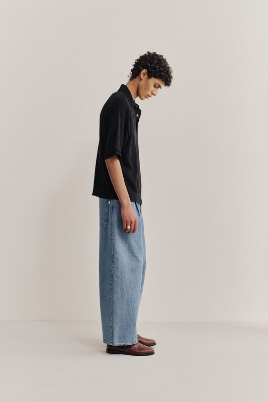 Men's knit short-sleeved polo shirt, black, paired with wide-leg light wash denim jeans and brown leather Fano slippers.