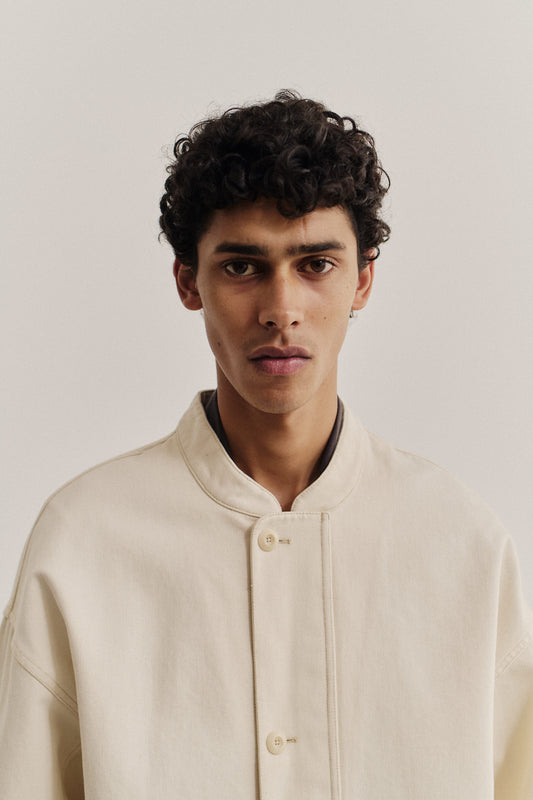Men's outerwear jacket, off-white organic cotton raw denim, boxy fit, stand-up collar, buttoned front.