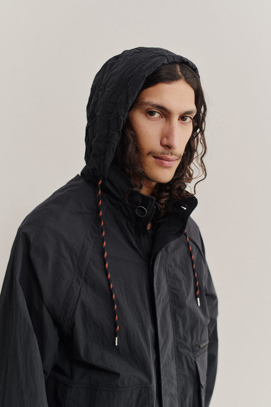 Men's outerwear, Zambezi Fisher Jacket in black recycled nylon and cotton blend, with hood and orange-tipped drawstrings.