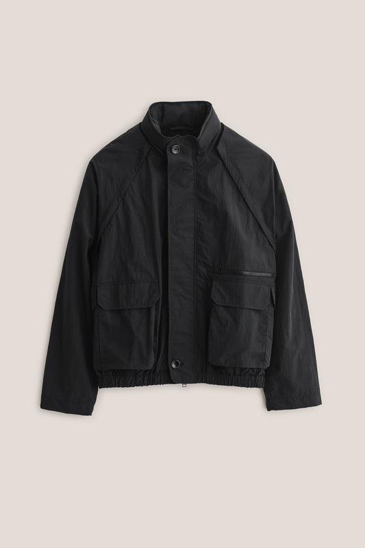 Men's outerwear jacket, black recycled nylon cotton blend, wide silhouette, deep raglan sleeves, bellows pockets.