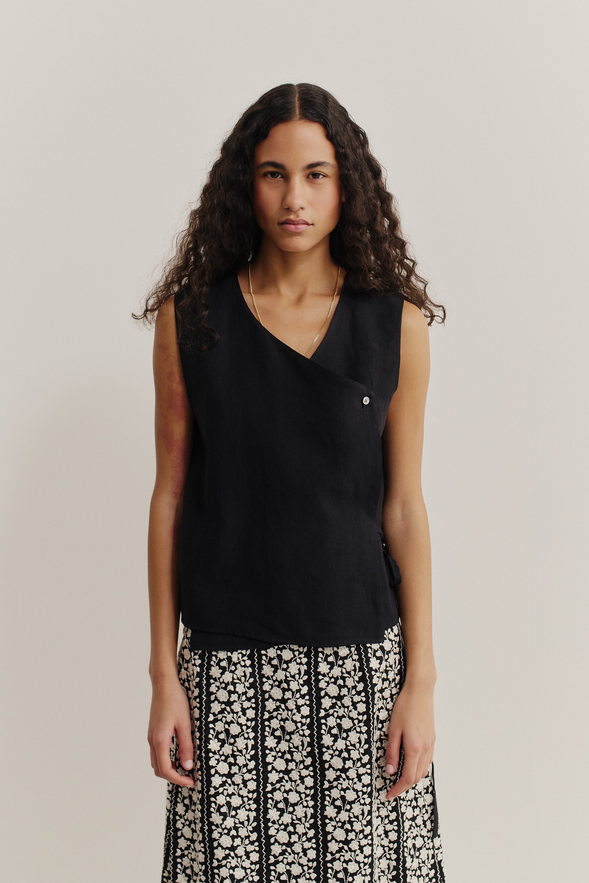 Women's sleeveless shirt, black linen, asymmetric wrap front with button and tie closure.