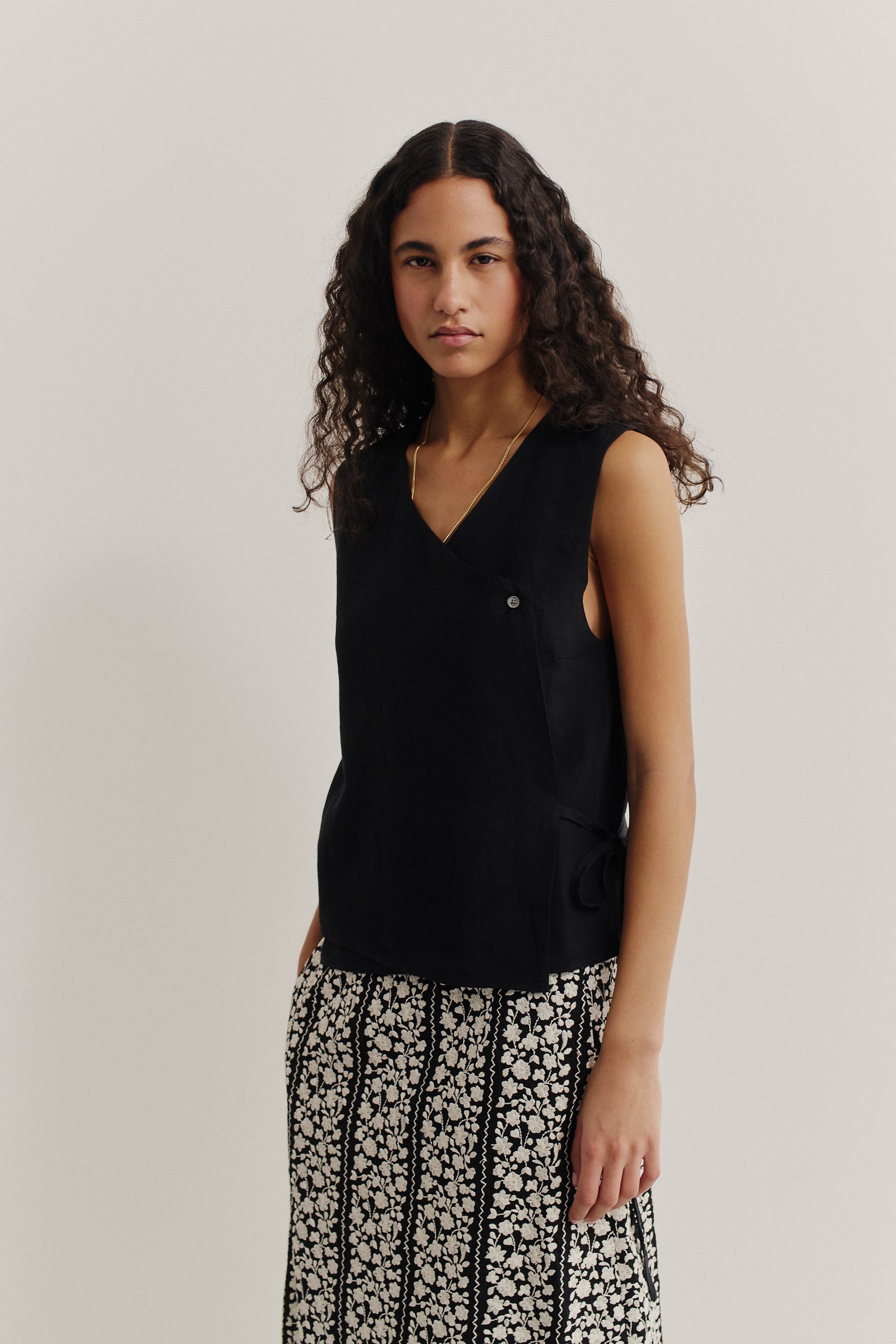 Women's sleeveless wrap shirt in black linen, featuring an asymmetric V-neck and side tie.