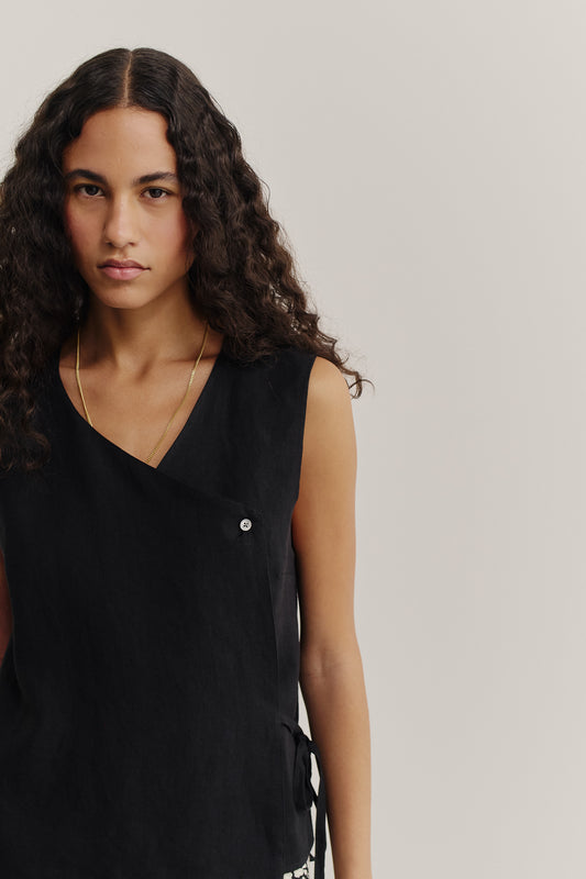 Women's sleeveless wrap shirt in black linen, featuring an asymmetric V-neck and side tie.