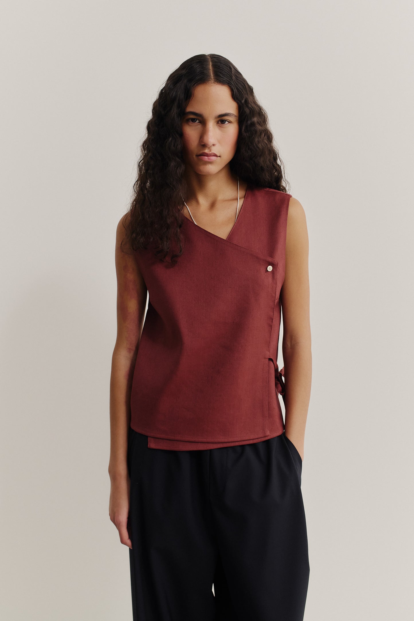 Women's sleeveless wrap shirt in linen-virgin wool-mohair blend, featuring an asymmetric front, V-neck, and button closure in dark red.