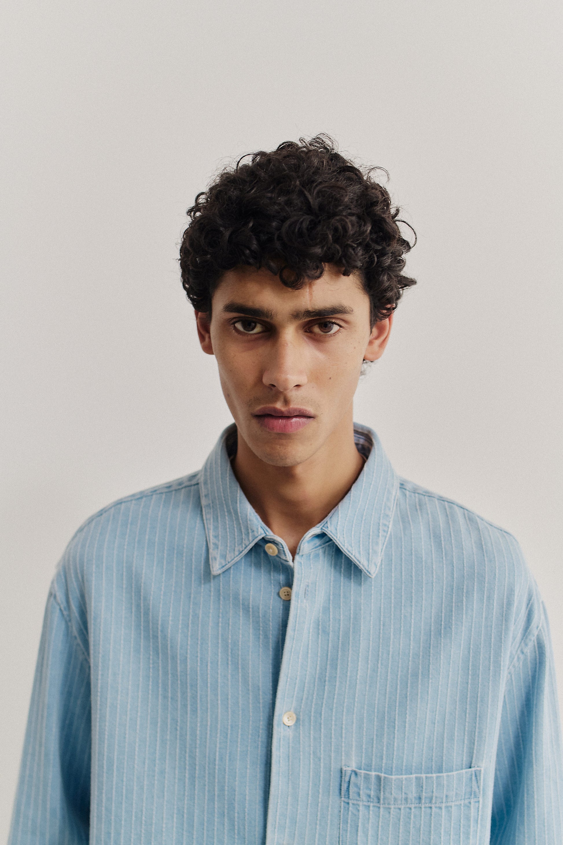 Men's long-sleeved shirt, organic cotton denim, washed light blue with subtle white pinstripes, oversized fit.