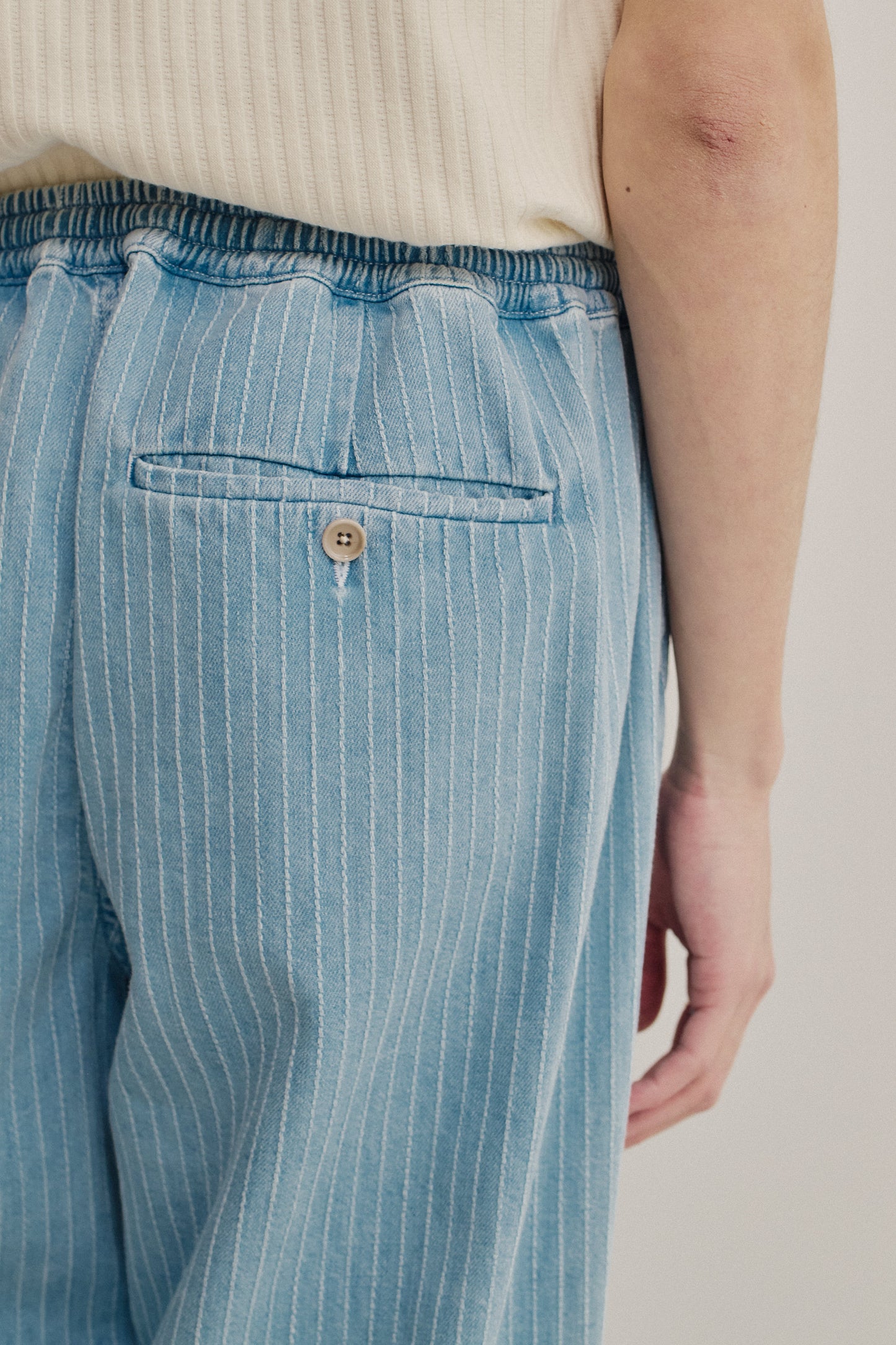 Men's long-pants, organic cotton denim, washed light blue with white pinstripes, elastic waist, and buttoned back welt pocket.