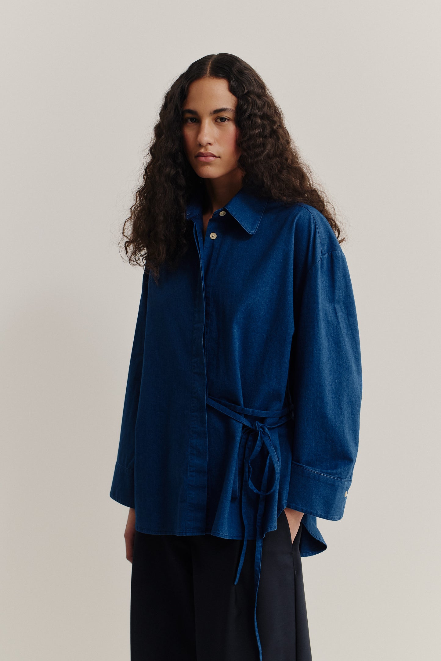 Women's long-sleeved shirt, washed indigo cotton, oversized fit, curved hem, and waist tie.