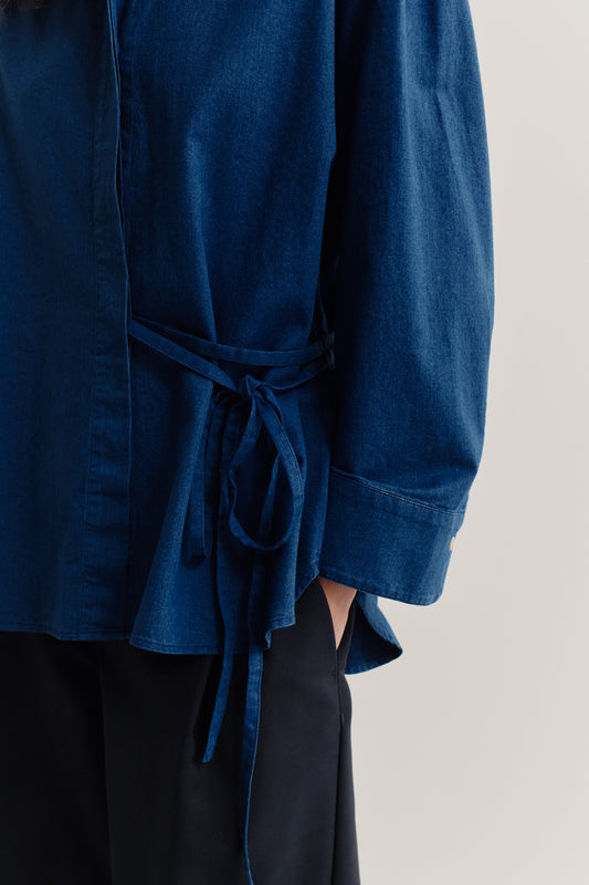 Women's long-sleeved shirt, washed indigo cotton, wide oversized fit, curved hem, tie-waist detail.