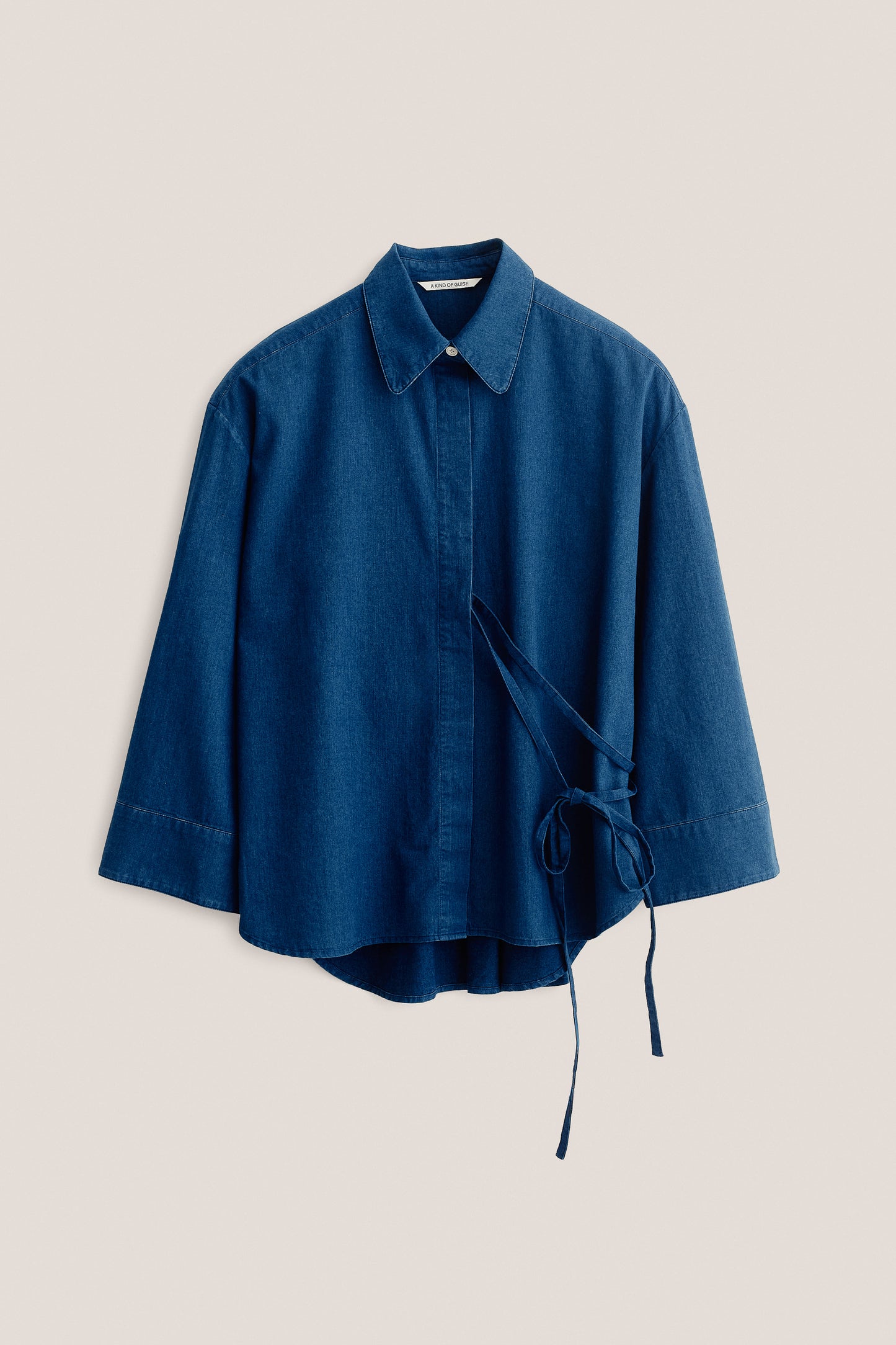 Women's long-sleeved shirt, washed indigo cotton, wide oversized fit, curved hem, and side tie detail.